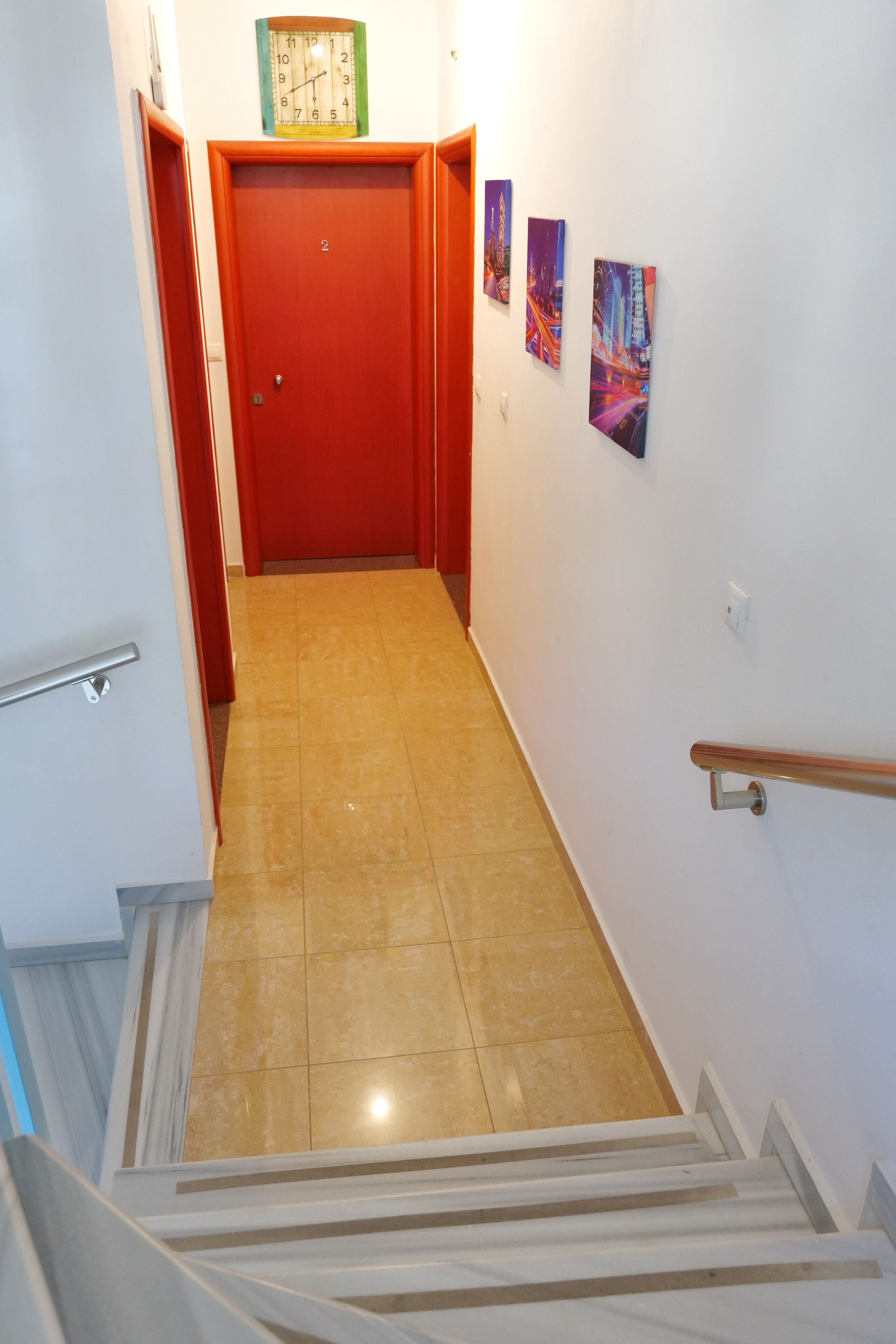 Un couloir avec une porte rouge, une horloge et trois tableaux encadrés accrochés au mur.