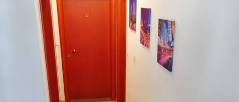 Un pasillo con una puerta roja, un reloj y tres cuadros en la pared.