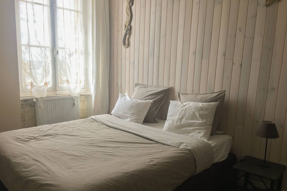 A bedroom with a bed, pillows, a bedside table, and a lamp.