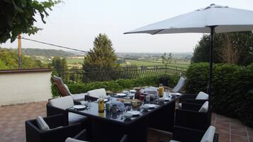 An outdoor patio with a table set for dining, surrounded by wicker chairs, and an umbrella providing shade.