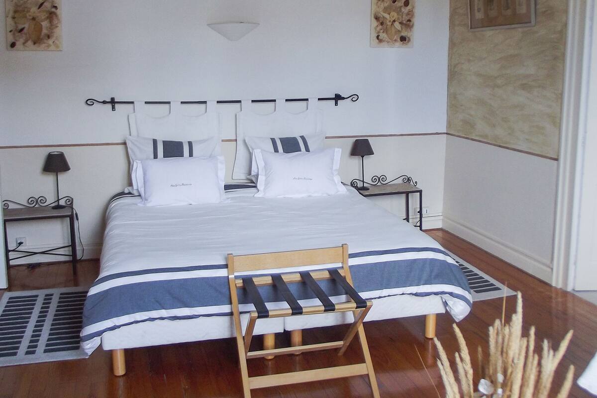 A neatly arranged bedroom with a bed, bedside tables, a chair, and a small table with a vase.