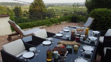 An outdoor dining area with a table set for breakfast, overlooking a scenic landscape.