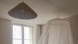 A bedroom with a canopy bed, a hanging light fixture, and a window with curtains. - Les Gués Rivières (Pujols)
