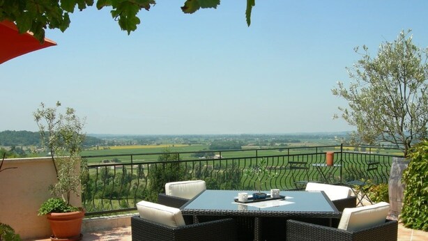 A terrace with a table and chairs, a potted plant, and a view of a green landscape. - Les Gués Rivières (Pujols)
