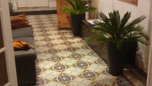 A hallway with patterned tiles, a reception desk, potted plants, and a painting on the wall. - Les Gués Rivières (Pujols)