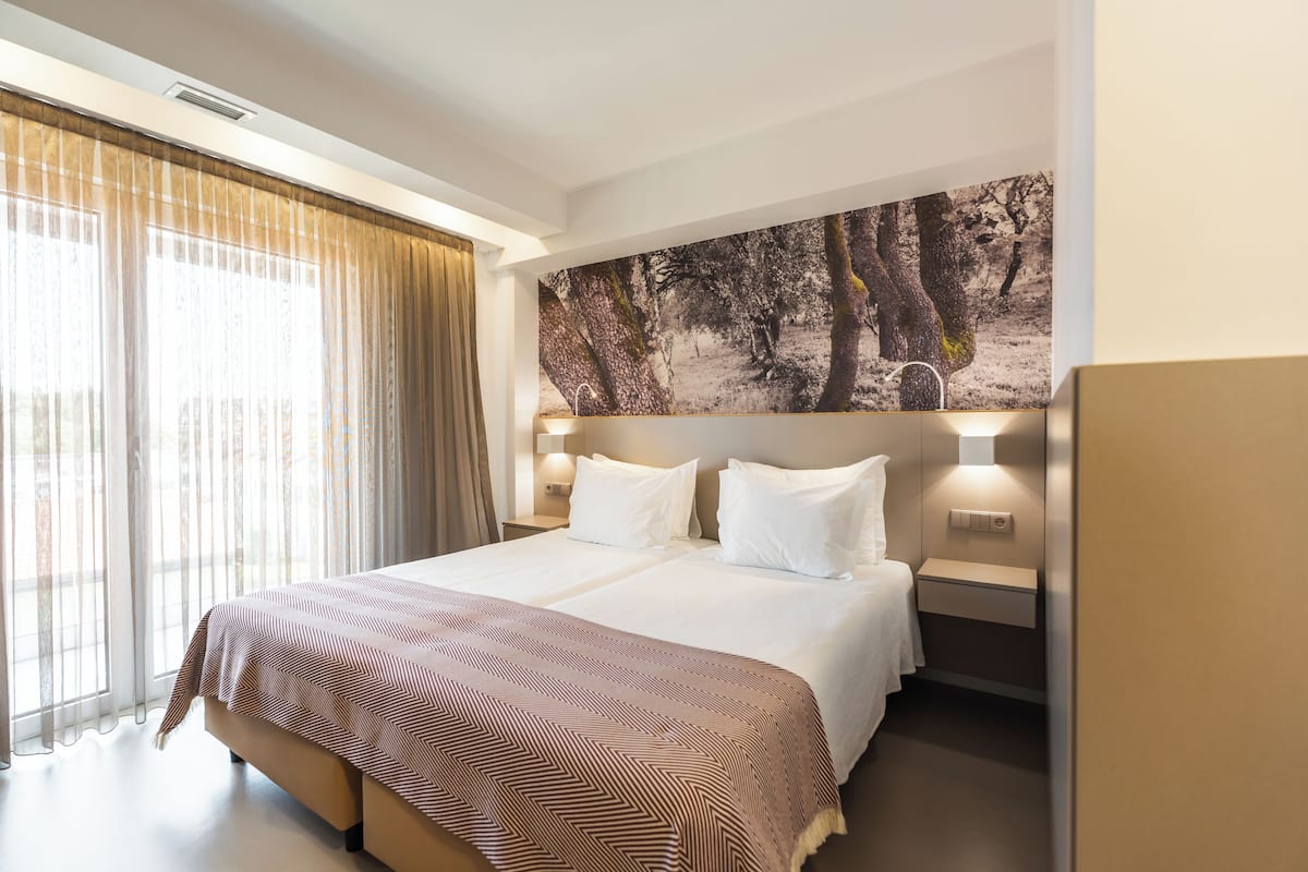 A hotel room with a large bed, a wall-mounted TV, and a window with curtains.