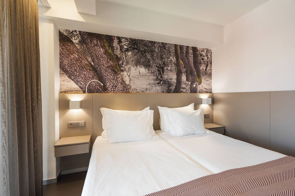 A hotel room with a large bed, two bedside tables, and a wall-mounted light fixture.