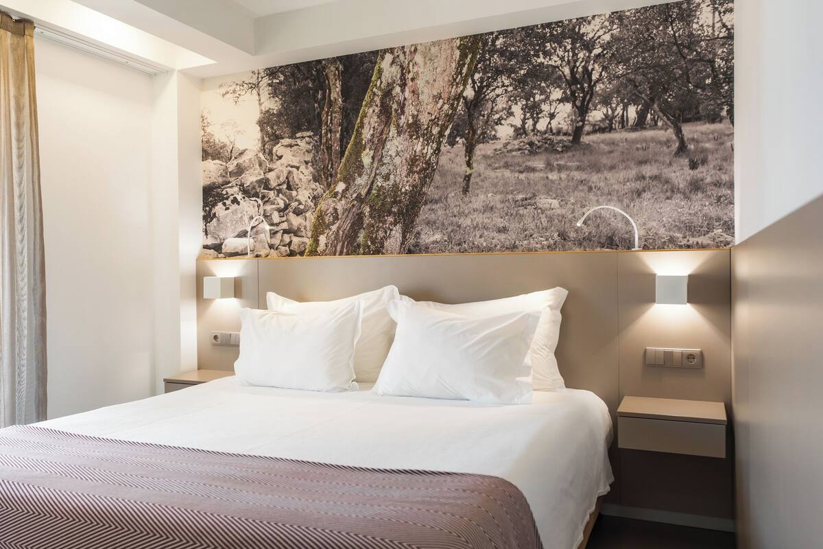A hotel room with a large bed, two bedside tables with lamps, and a large nature-themed artwork on the wall.