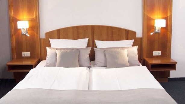 A hotel room with a large bed, two bedside tables, and wall-mounted lamps. - Hotel Germania (Reutlingen)