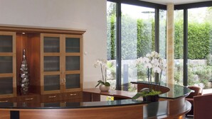 A modern reception area with a curved wooden counter, glass display cabinets, and a large window offering a view of greenery. - Hotel Germania (Reutlingen)