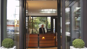 A hotel reception area with a receptionist, a wooden reception desk, and a glass entrance. - Hotel Germania (Reutlingen)