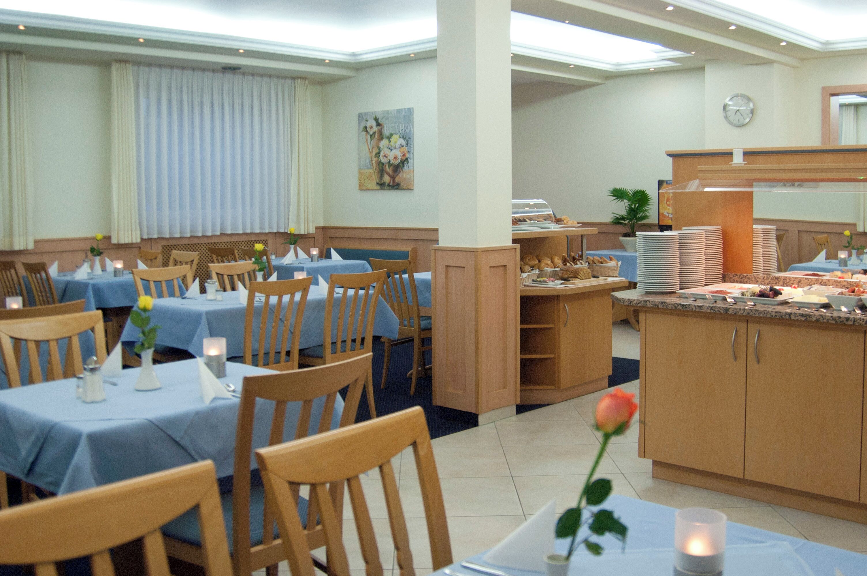 Un comedor de hotel con mesas dispuestas para los huéspedes, una estación de buffet y un reloj en la pared.