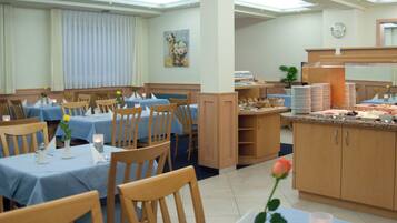 Un comedor de hotel con mesas dispuestas para los huéspedes, una estación de buffet y un reloj en la pared.