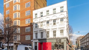 A multi-story building with a mix of brick and white facades, a red storefront, and a white van parked on the street. - Drayton (London)