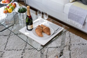 Una mesa de vidrio con una botella de Moët & Chandon, dos copas, un plato con cruasanes y una bandeja de frutas.