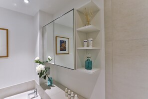 Un baño moderno con un espejo grande, un lavabo blanco y un estante con artículos de tocador.