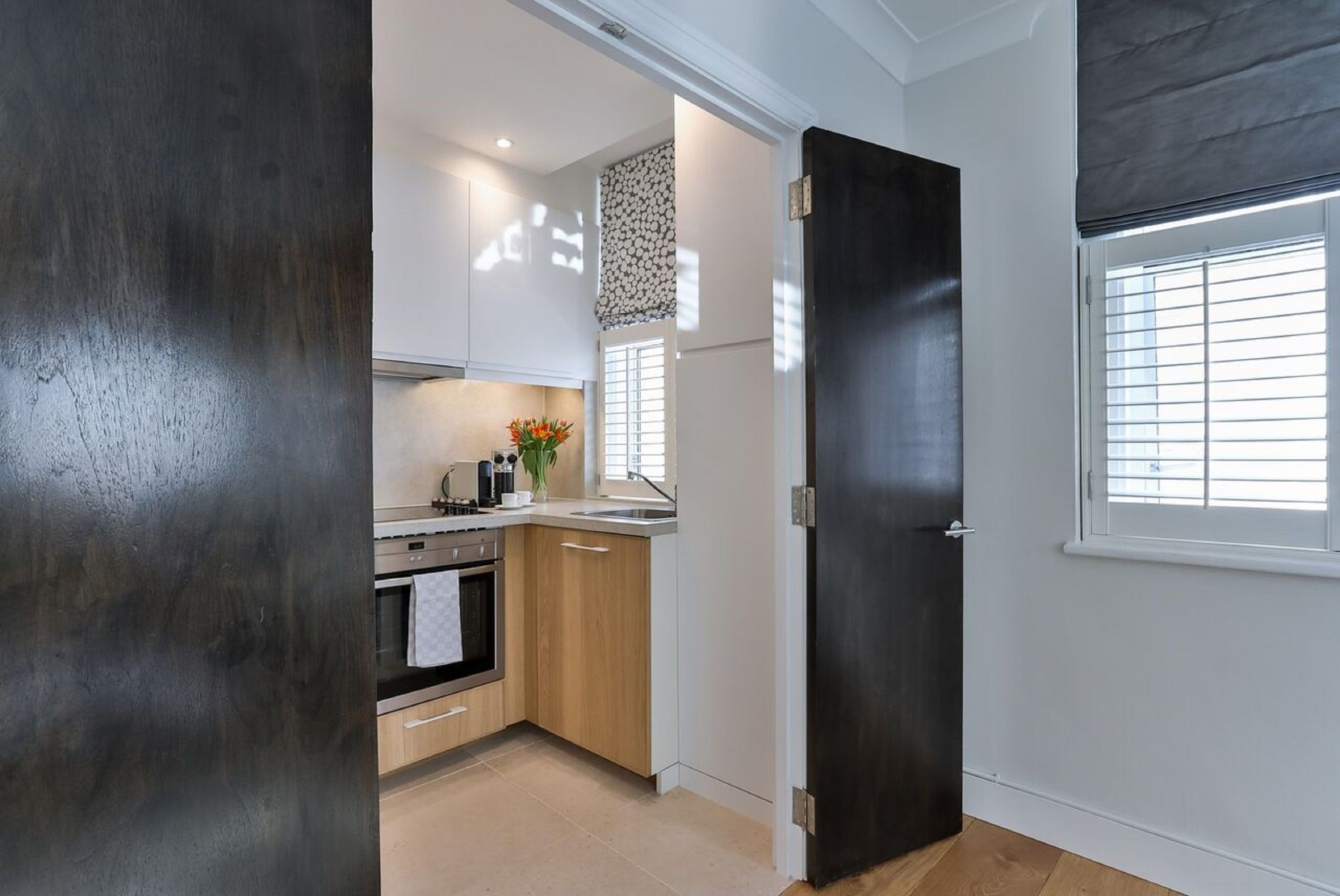 A compact kitchen with a dark door, a window with blinds, and a light-colored floor.