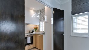 A compact kitchen with a dark door, a window with blinds, and a light-colored floor. - Drayton (London)