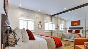 A modern bedroom with a large bed, a glass partition, and a view of another room. - Drayton (London)
