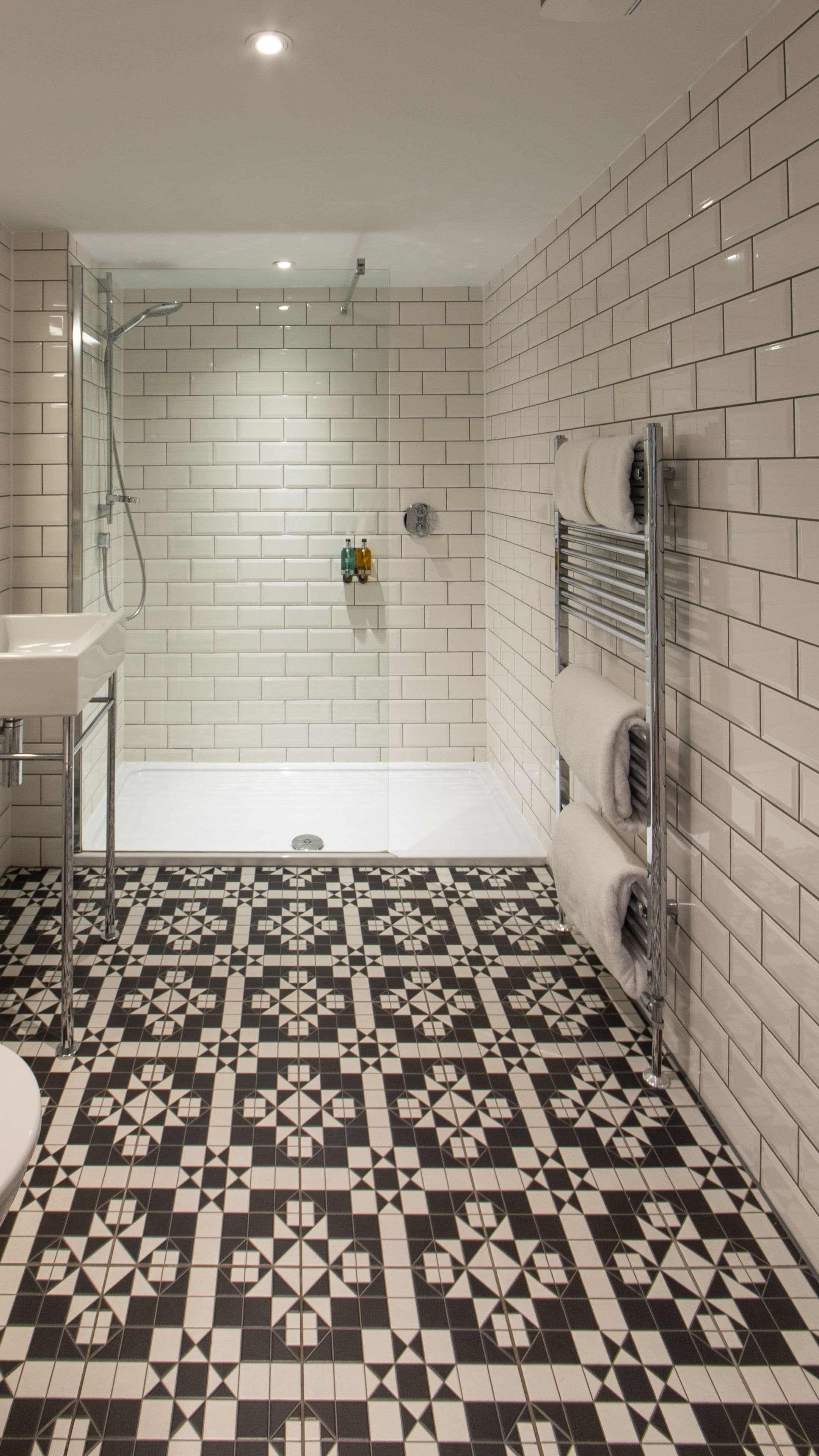 A bathroom with a shower, a sink, and a toilet. The floor has a geometric tile pattern.