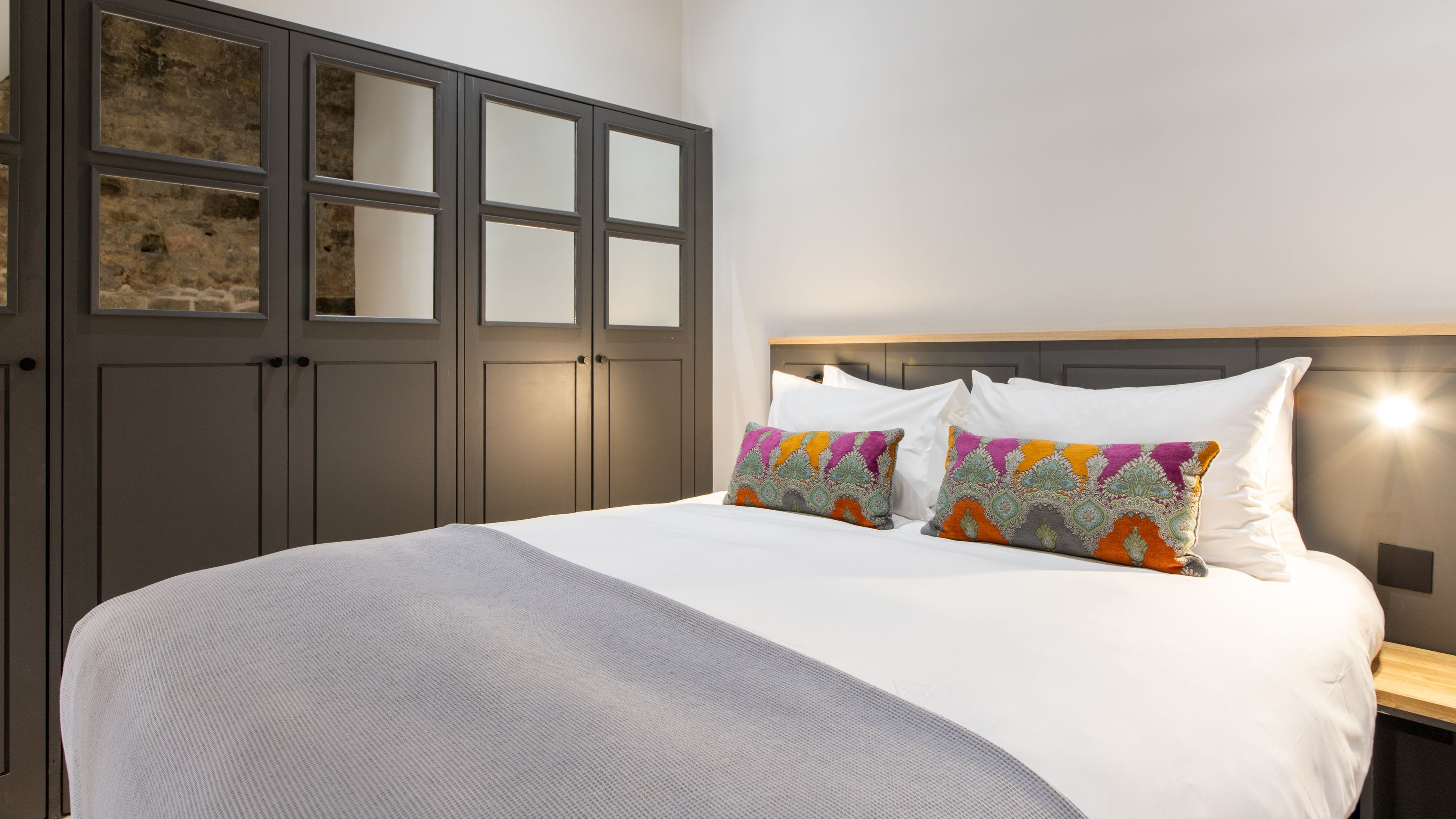 A bedroom with a large bed, a wardrobe with mirrored doors, and a headboard with built-in lighting.