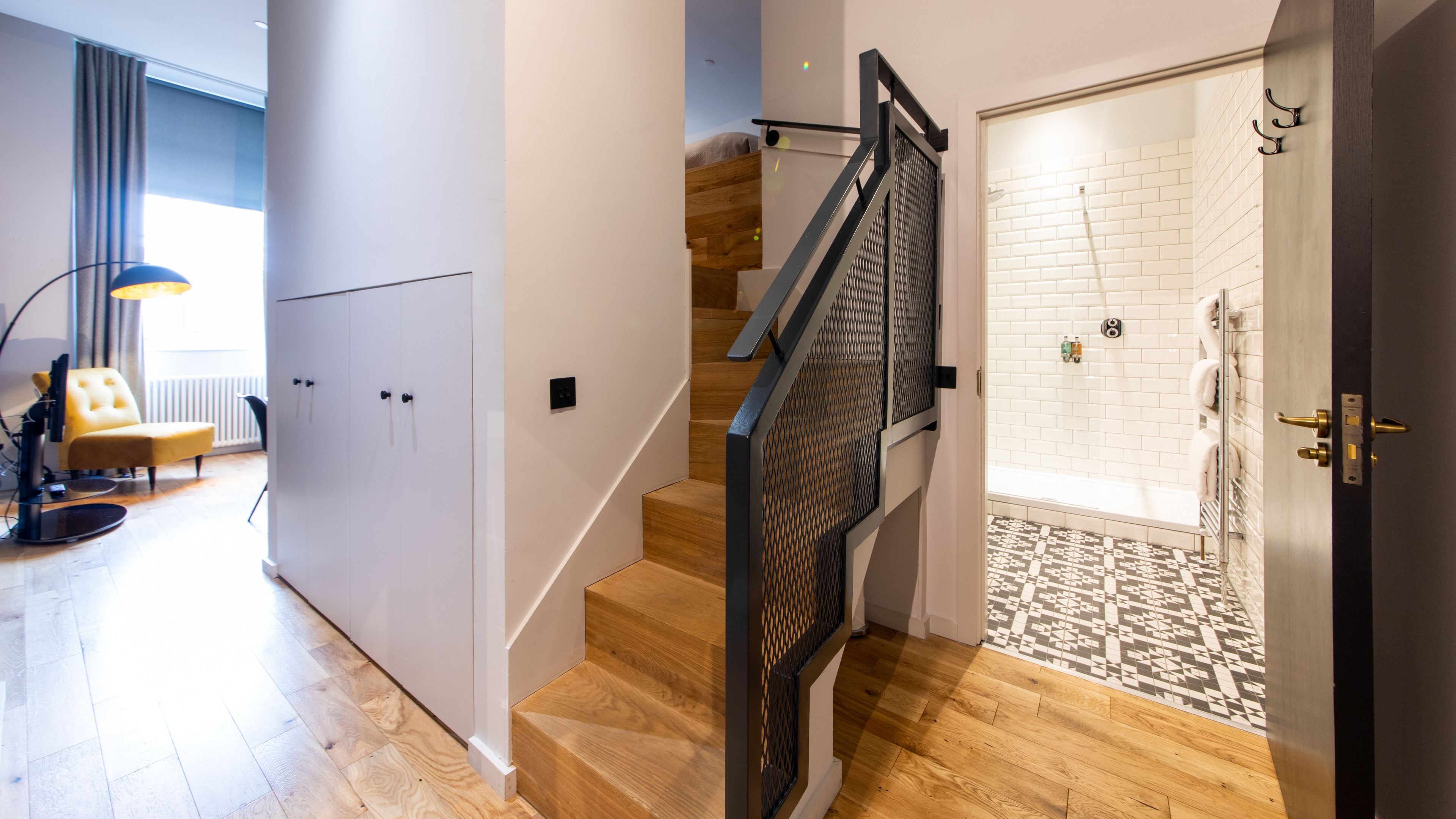 A modern interior with a wooden staircase, a glass shower area, and a seating area with a chair and lamp.