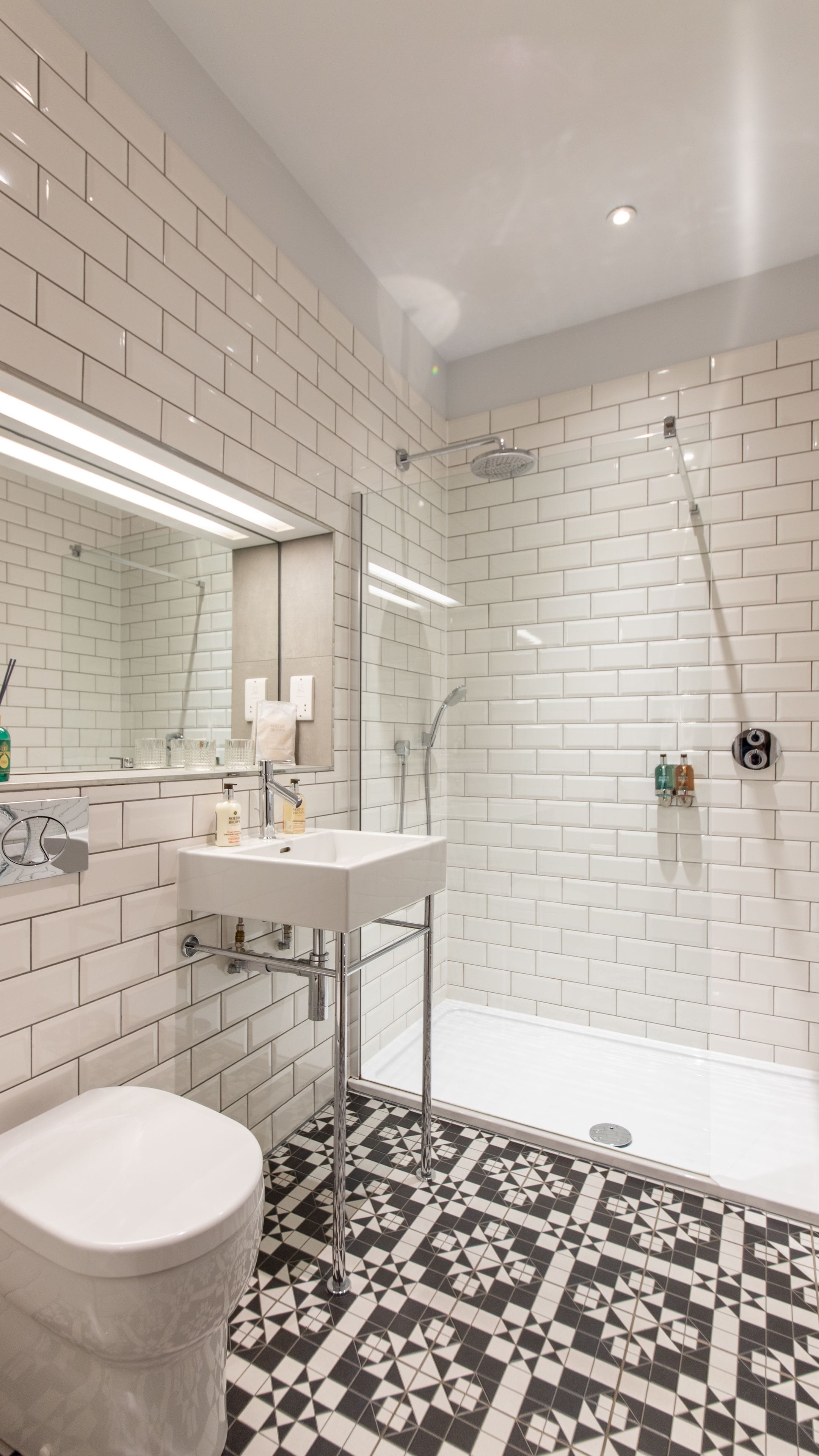 A modern bathroom with white subway tiles, a glass-enclosed shower, a white sink, and a toilet.
