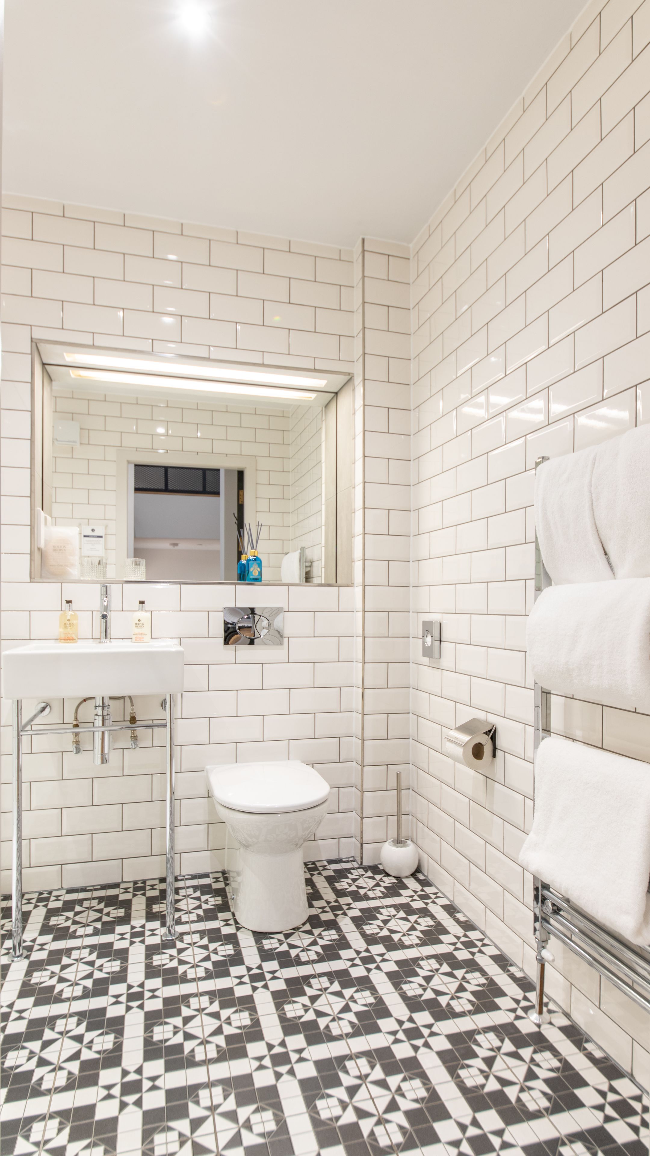 Ein Badezimmer mit weißen Fliesen im U-Bahn-Stil, einer Toilette, einem Waschbecken und einem Spiegel.