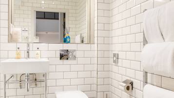 Un baño con azulejos blancos tipo metro, inodoro, lavamanos y espejo.