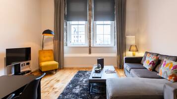 Un salon moderne avec un téléviseur à écran plat, un fauteuil jaune, un canapé gris agrémenté de coussins à motifs, un lampadaire noir et une fenêtre avec des rideaux.