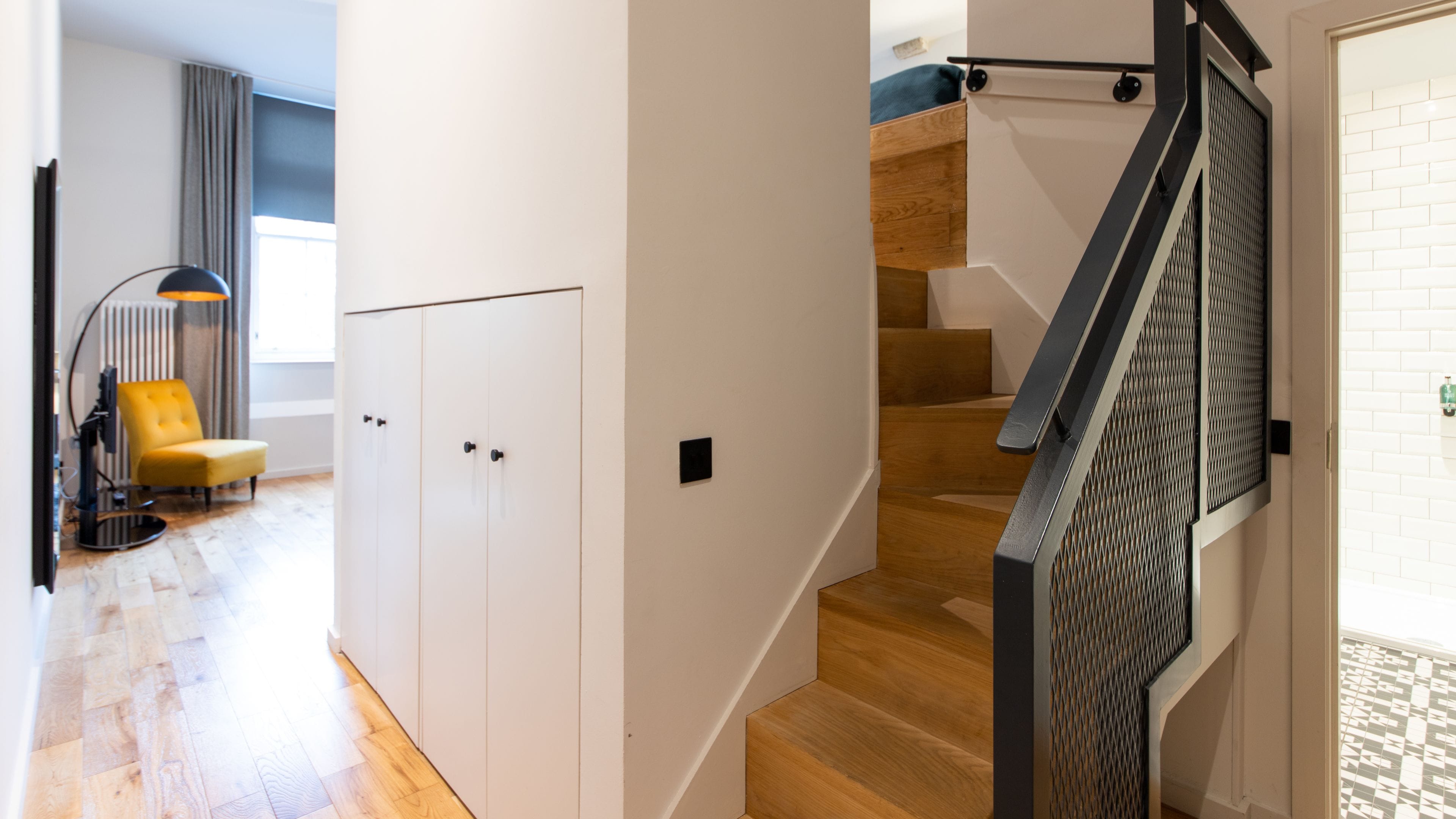 Un interior moderno con una escalera, piso de madera y una silla amarilla.