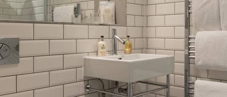 A bathroom with white subway tiles, a white sink, a mirror, a towel rack, and a toilet.