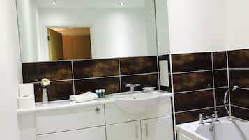 A modern bathroom with a white vanity, a large mirror, a bathtub, and dark brown tiles.