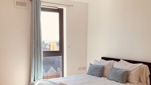 A bedroom with a bed, a window with curtains, a bedside table, and a view of a building outside. - SFA New Central Woking (Woking)