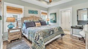 A bedroom with a wooden bed, two bedside tables with lamps, a ceiling fan, and a large window with blinds.