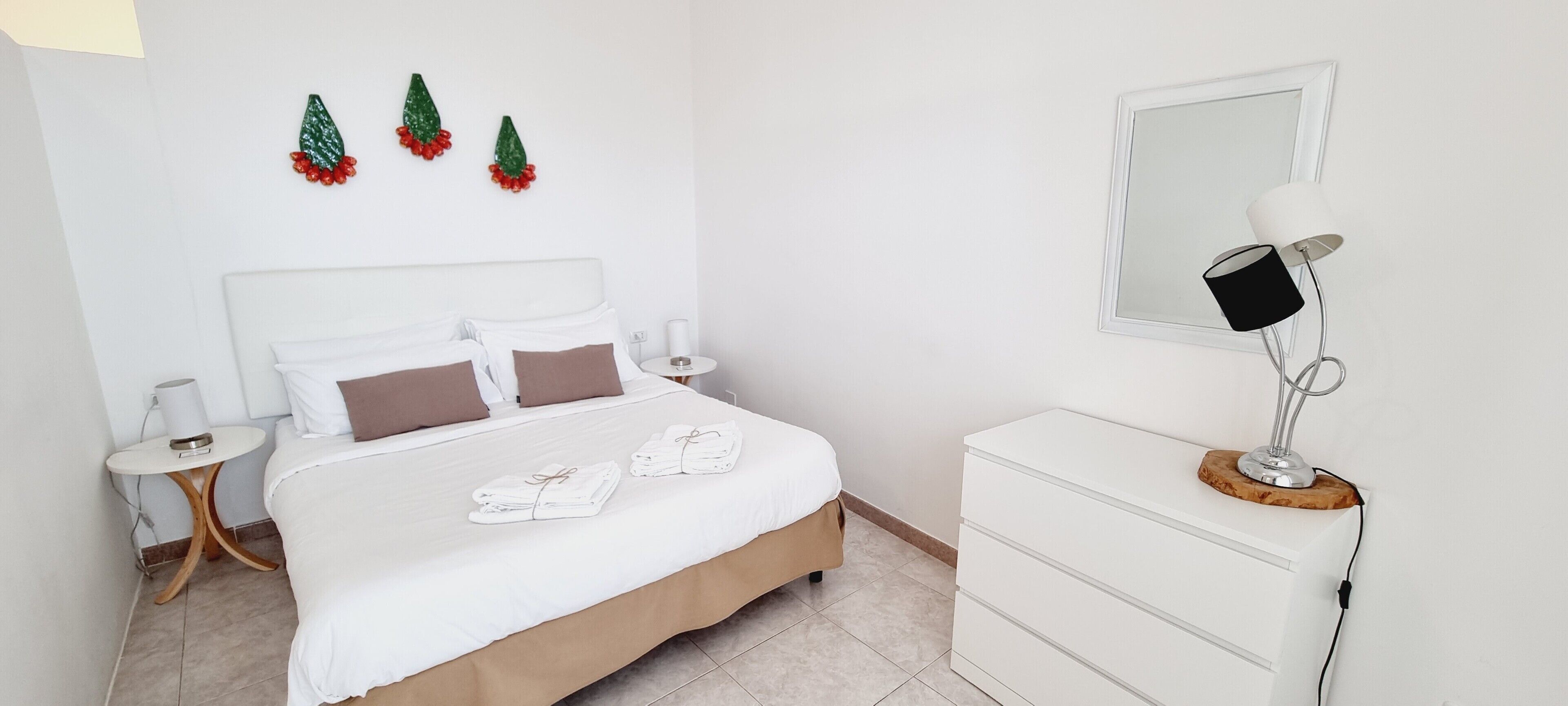 Ein ordentlich eingerichtetes Schlafzimmer mit Bett, Nachttischen, einem Schminktisch und Wandbildern.