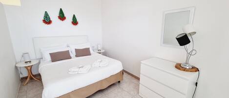 Ein ordentlich eingerichtetes Schlafzimmer mit Bett, Nachttischen, einem Schminktisch und Wandbildern.