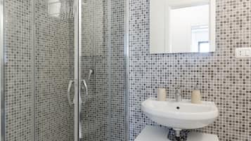 A bathroom with a glass-enclosed shower, a white sink with a mirror above it, and a tiled wall.
