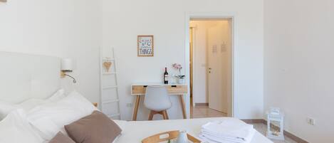 A hotel room with a bed, a desk, a chair, a tray with flowers, and a small table with a cup and a bowl.