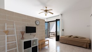 A modern living room with a flat-screen TV, a wooden bench, a white shelving unit, a ceiling fan, and a beige sofa. - Biancaleuca Rooms & Suite (Castrignano del Capo)