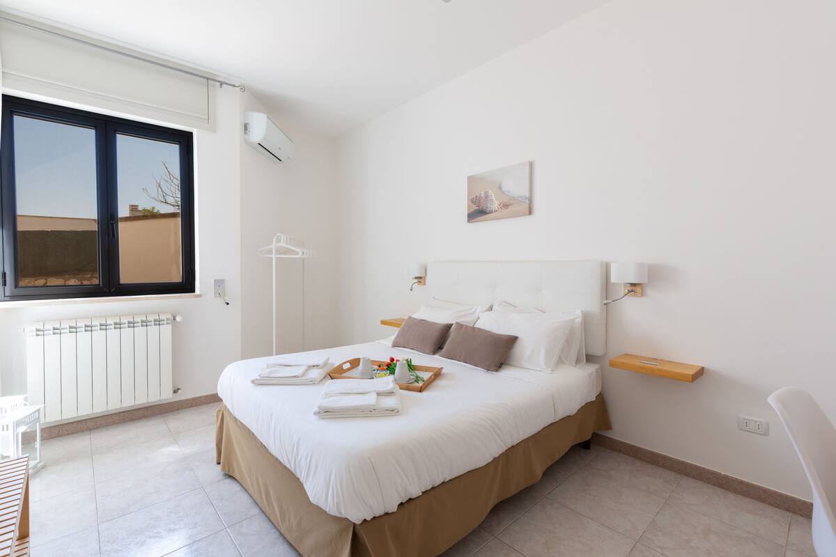 A neatly arranged bedroom with a large bed, a bedside table, a window, and a radiator.