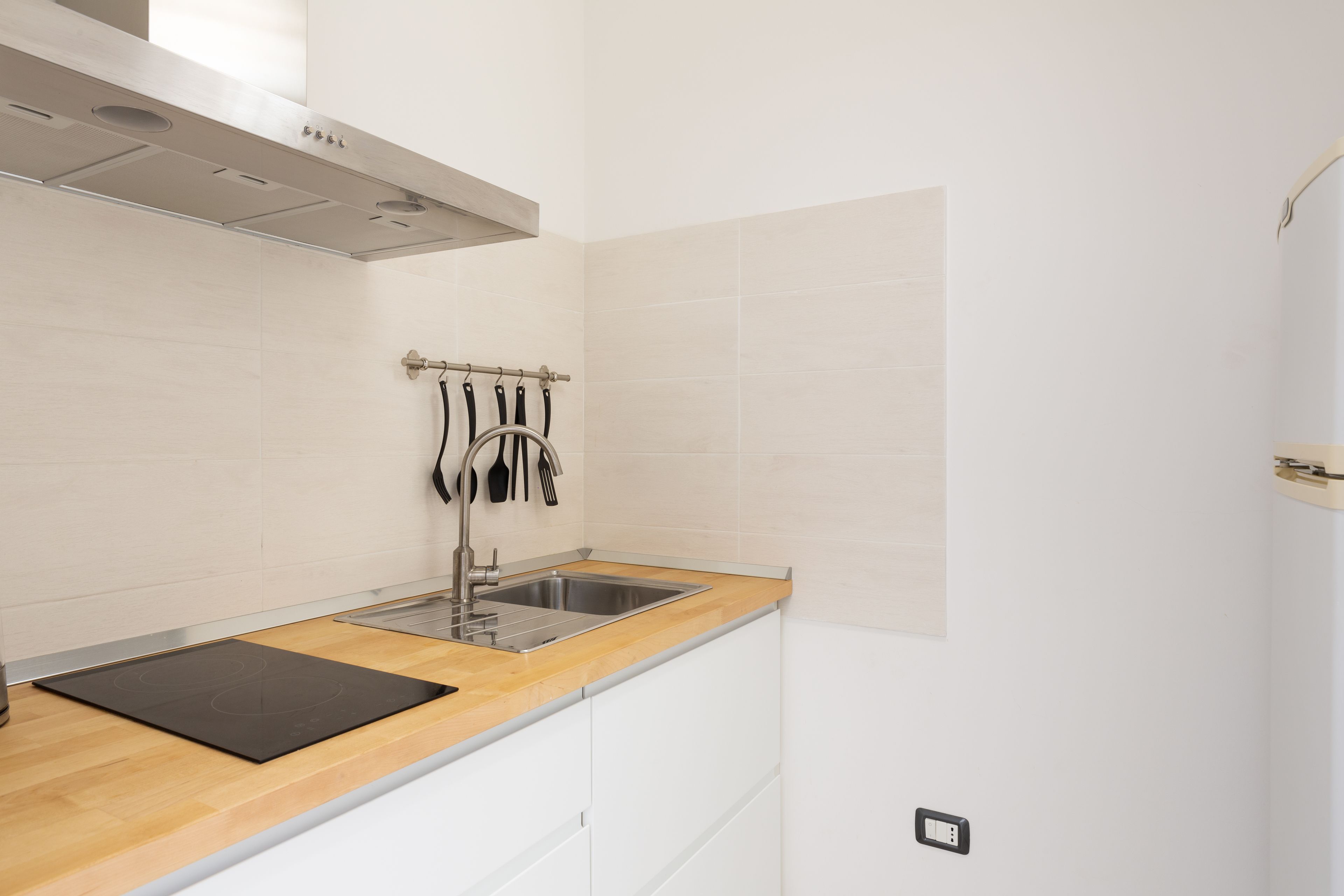 A modern kitchen with a wooden countertop, stainless steel sink, and white cabinetry.