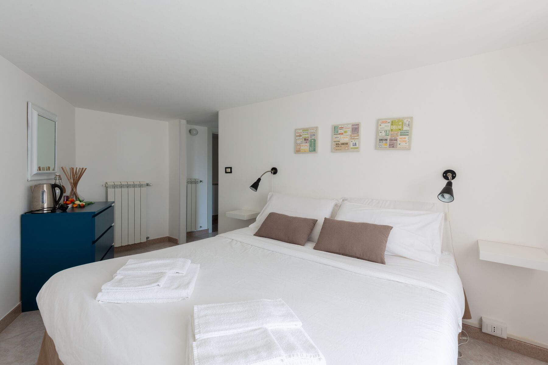 Una habitación de hotel con cama, escritorio, espejo, radiador y adornos en la pared.