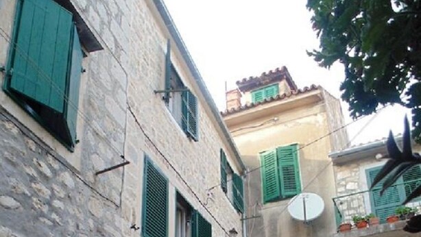 A narrow street with stone buildings, green shutters, and potted plants. - Guest House Petricevic (Split)