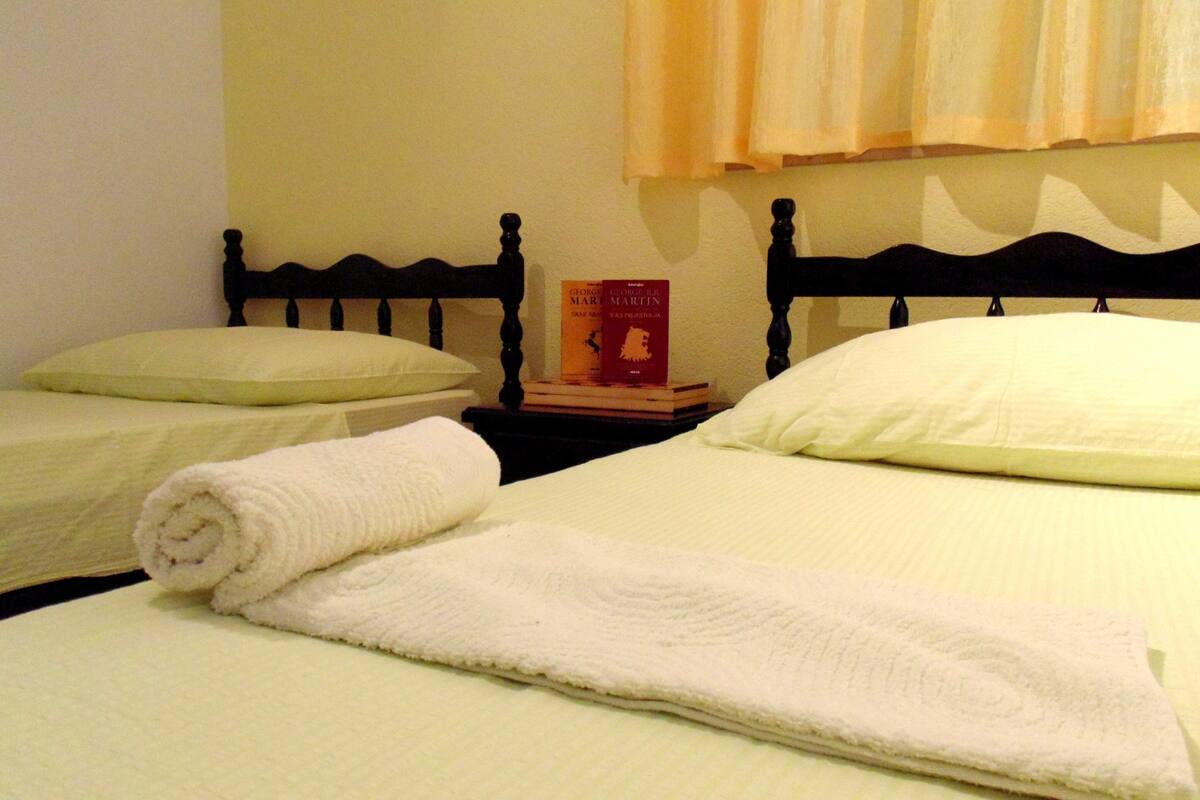 A hotel room with two beds, each with a white pillow and a rolled white towel. There is a book on a nightstand between the beds.
