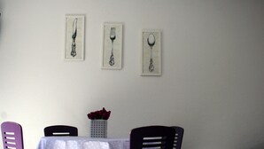 A dining area with a table and chairs, a vase with flowers, and three framed utensils on the wall. - Guest House Petricevic (Split)