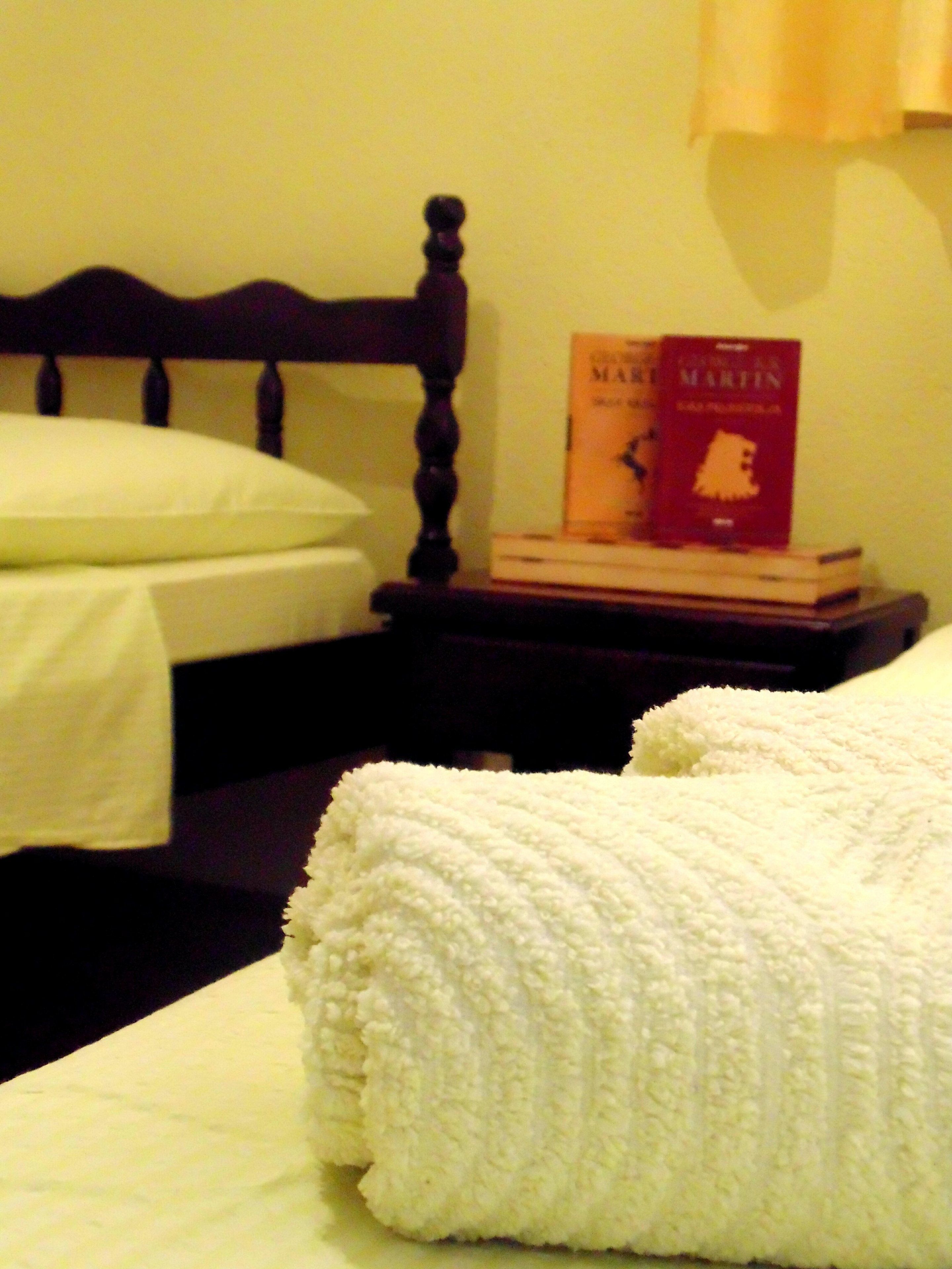 A neatly made bed with a white blanket, a wooden headboard, and a bedside table with books.