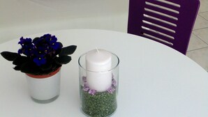 A room with a white sofa, purple pillows, a purple chair, a white table with a glass candle holder and a potted plant. - Guest House Petricevic (Split)