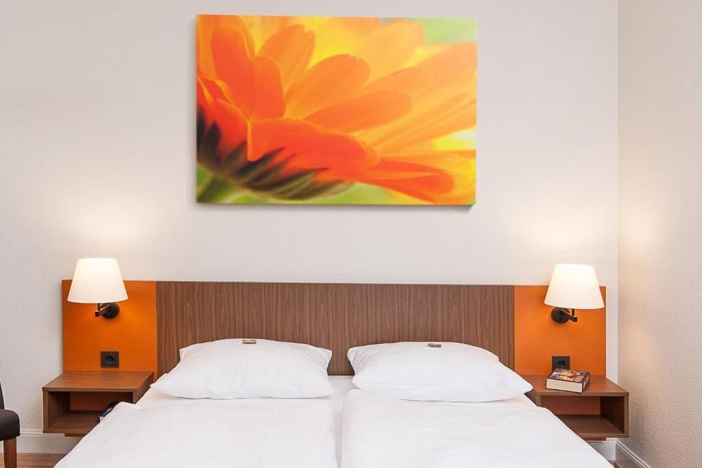 A hotel room with two beds, nightstands with lamps, and a wall-mounted painting.