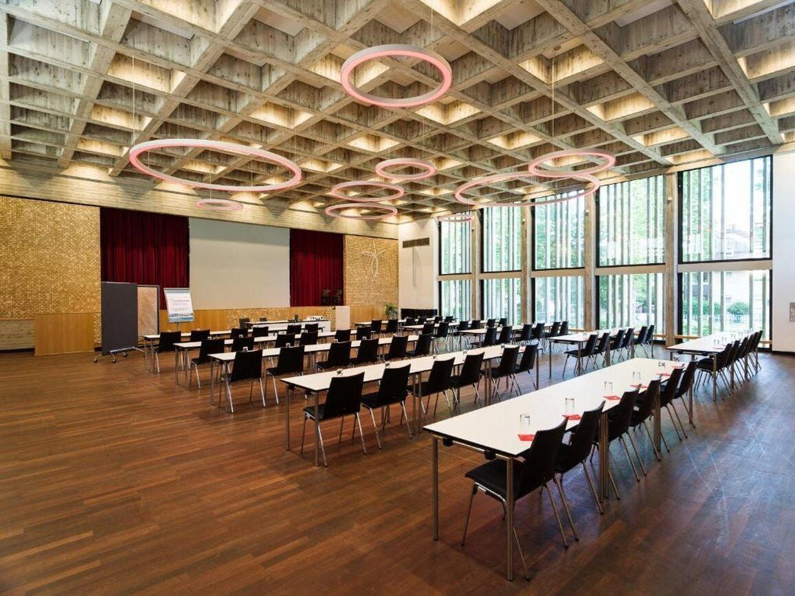 A conference room with a wooden ceiling, large windows, and a stage with a red curtain.
